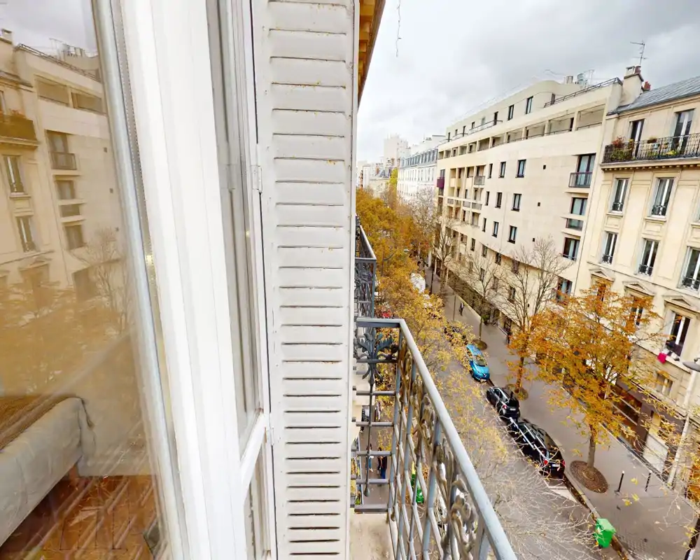 Piccolo balcone in stile parigino con ringhiera in ferro battuto che affaccia su una strada alberata, perfetto per il caffè mattutino.