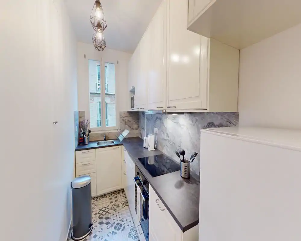 Cucina moderna a corridoio, luminosa, con mobili bianchi, piani scuri, piastrelle a motivo e elettrodomestici integrati — perfetta per appartamenti urbani compatti.