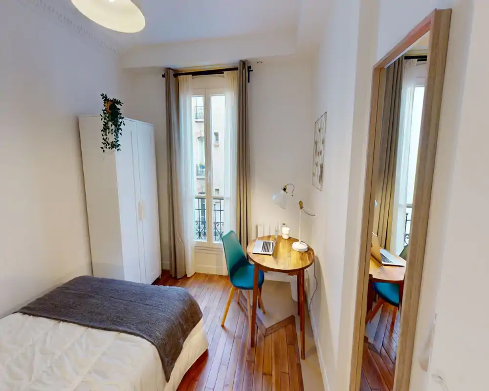 Chambre lumineuse et chaleureuse avec lit double, parquet, armoire et un petit espace de travail près de la fenêtre — idéale pour se détendre ou travailler à distance.