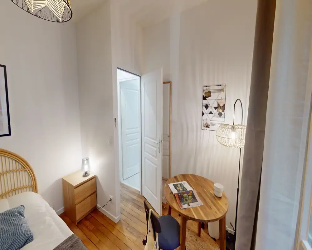 Camera da letto luminosa e accogliente con testiera in rattan, comodino in legno e una piccola scrivania: illuminazione calda e toni naturali creano un ambiente ideale per affitti brevi.