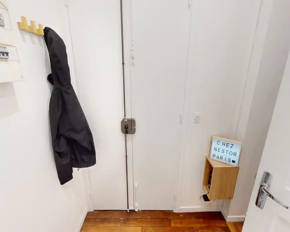 Ingresso compatto e luminoso con pavimento in legno, ganci a muro e una piccola mensola sospesa — pratico per giacche e chiavi.