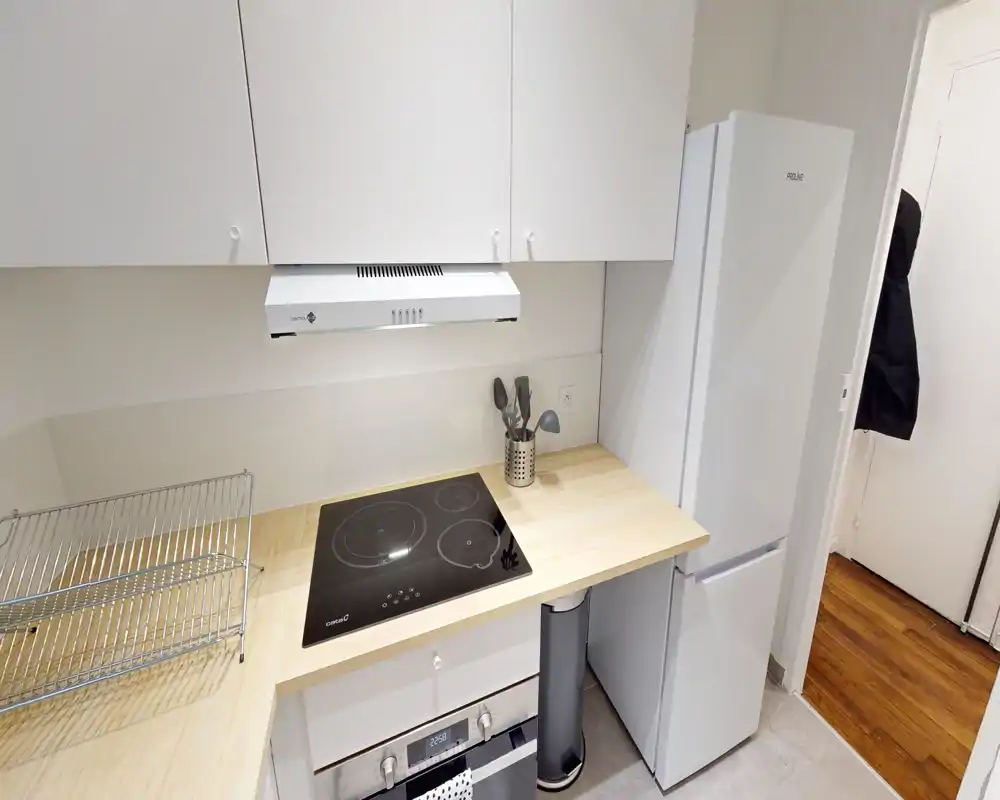 Cucina moderna compatta con piano ad induzione, cappa, frigorifero e piano in legno — luminosa, ordinata e funzionale per un piccolo appartamento.