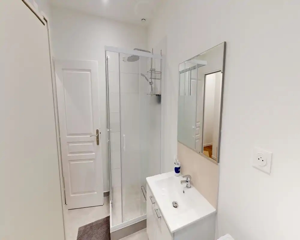 Bagno compatto e moderno con cabina doccia in vetro, lavabo con mobiletto bianco e specchio a parete. Finiture neutre e ambiente luminoso, ideale per affitti brevi.