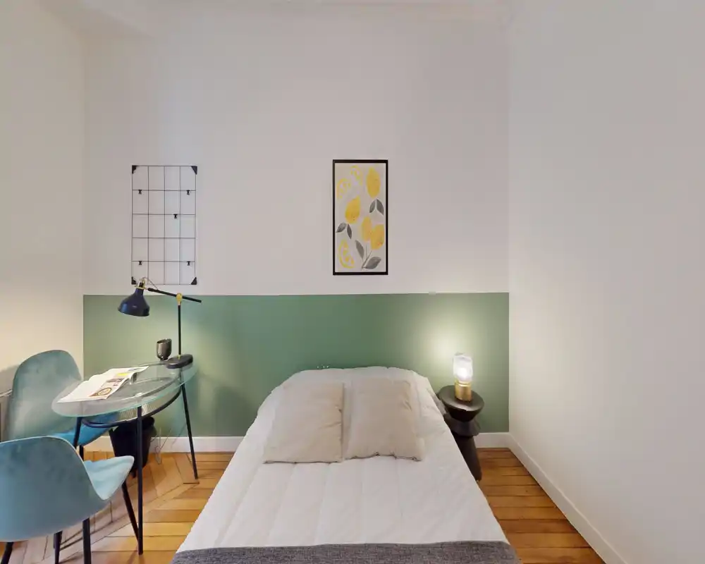 Chambre simple lumineuse et élégante avec lit bien fait, table de chevet avec lampe et un petit coin bureau — idéale pour un séjour confortable.
