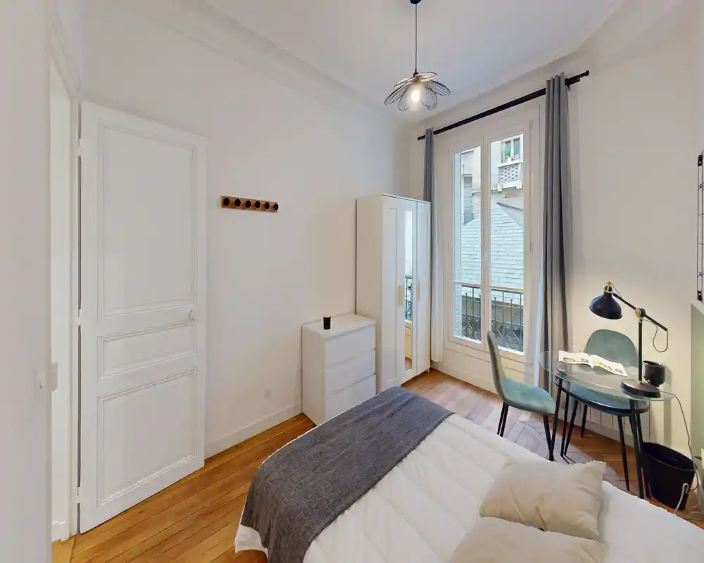 Chambre lumineuse et bien décorée avec lit double, textiles confortables et fenêtre apportant une belle lumière naturelle ; petit bureau et armoire visibles, idéale pour une location individuelle ou en couple.