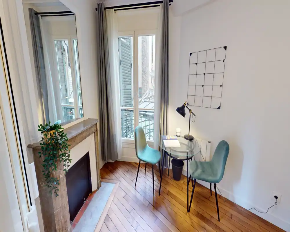 Coin repas/bureau lumineux et compact avec une table ronde en verre, deux chaises rembourrées et une fenêtre apportant lumière naturelle — idéal pour manger ou travailler chez soi.