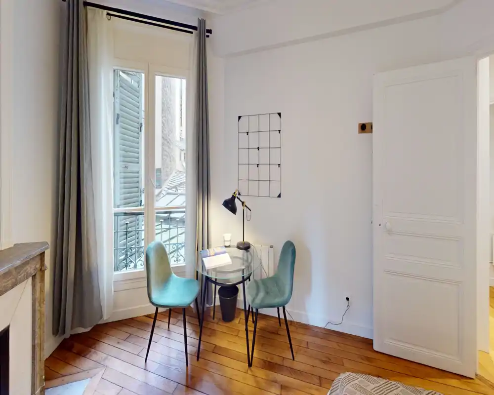 Espace de vie lumineux et élégant avec un coin repas/bureau près d'une grande fenêtre, rideaux doux, lampe décorative et parquet chaleureux — idéal pour un appartement en ville.