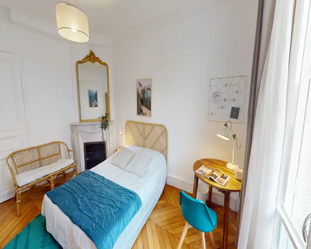 Dormitorio individual luminoso y con estilo, con cabecero de ratán, ropa de cama ordenada y un pequeño escritorio de madera junto a la ventana — ideal para una estancia cómoda.