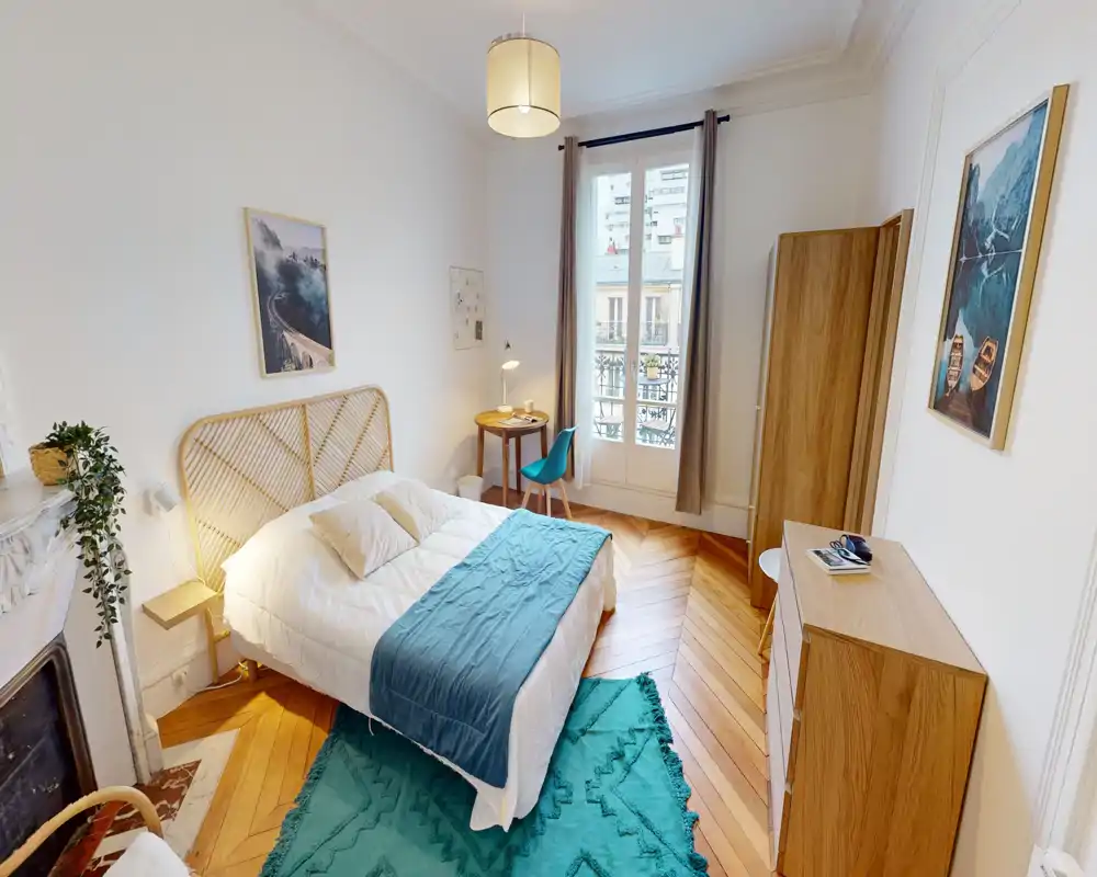 Dormitorio luminoso y con estilo con cama doble cómoda, acentos en turquesa y suelo de madera. Gran ventana que aporta mucha luz, con armario y escritorio.