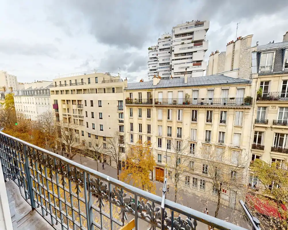 Balcón con vistas a una calle arbolada y edificios clásicos con rejas ornamentales — ideal para mostrar el espacio exterior del apartamento.