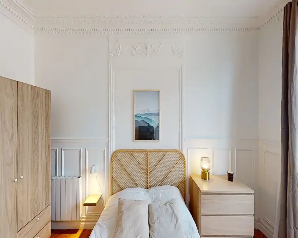 Dormitorio luminoso y elegante con cabecero de ratán, armario de madera y cómoda a juego; ropa de cama suave y lámpara de noche que aportan calidez.
