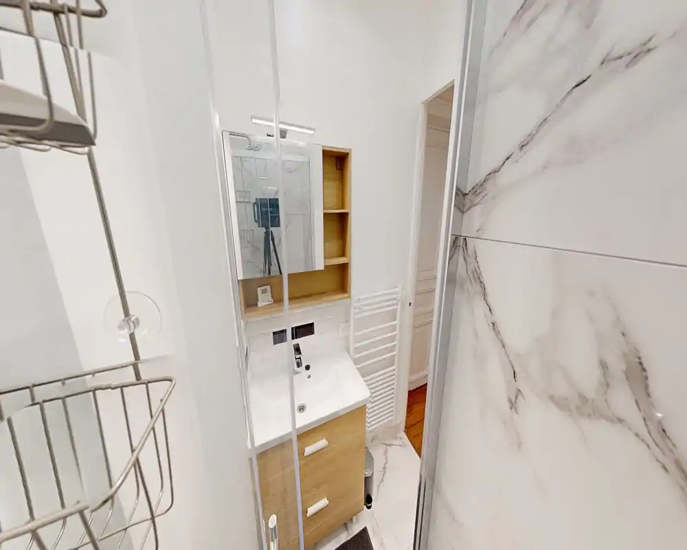Baño moderno y compacto con mueble de lavabo, armario con espejo, toallero calefactor y azulejos efecto mármol; luminoso y bien cuidado.