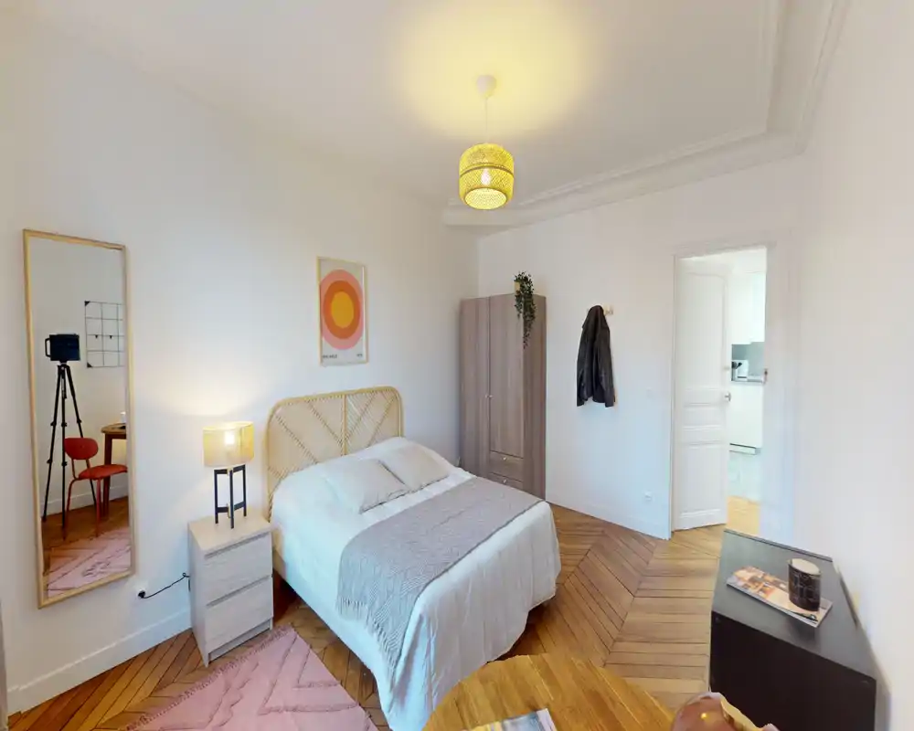 Camera da letto luminosa e ben arredata con testiera in rattan, tessili accoglienti, lampada da comodino e pavimento in legno a spina di pesce — perfetta per annunci che puntano su comfort e design.