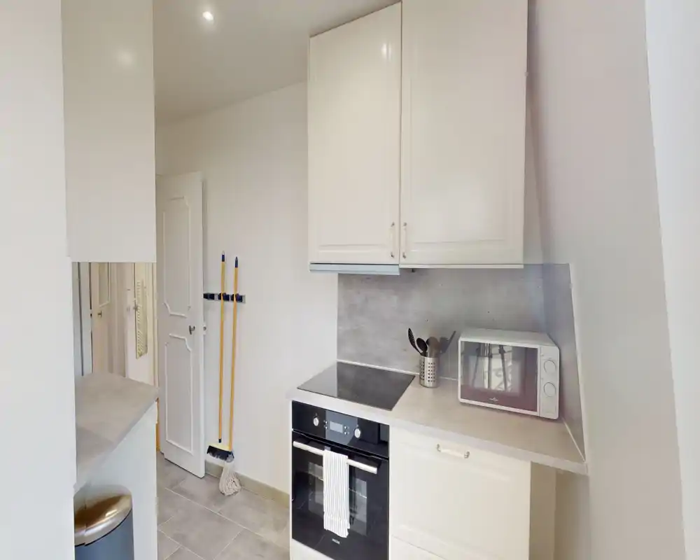 Cucina moderna compatta con forno incorporato, piano a induzione e microonde su un piano ordinato; mobili chiari e finiture neutre creano un ambiente luminoso e minimalista.