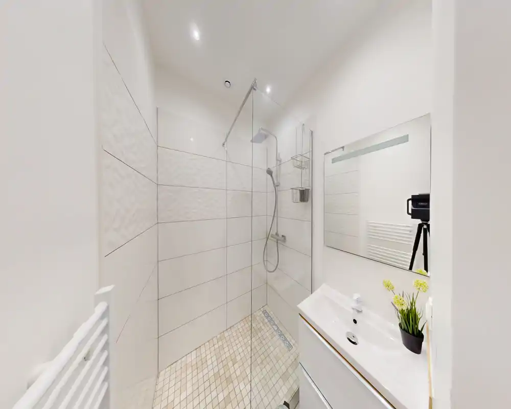 Bagno moderno e luminoso con doccia walk-in in vetro, soffione e doccetta, pavimento e pareti piastrellati, lavabo con cassetto e grande specchio — compatto e di design.