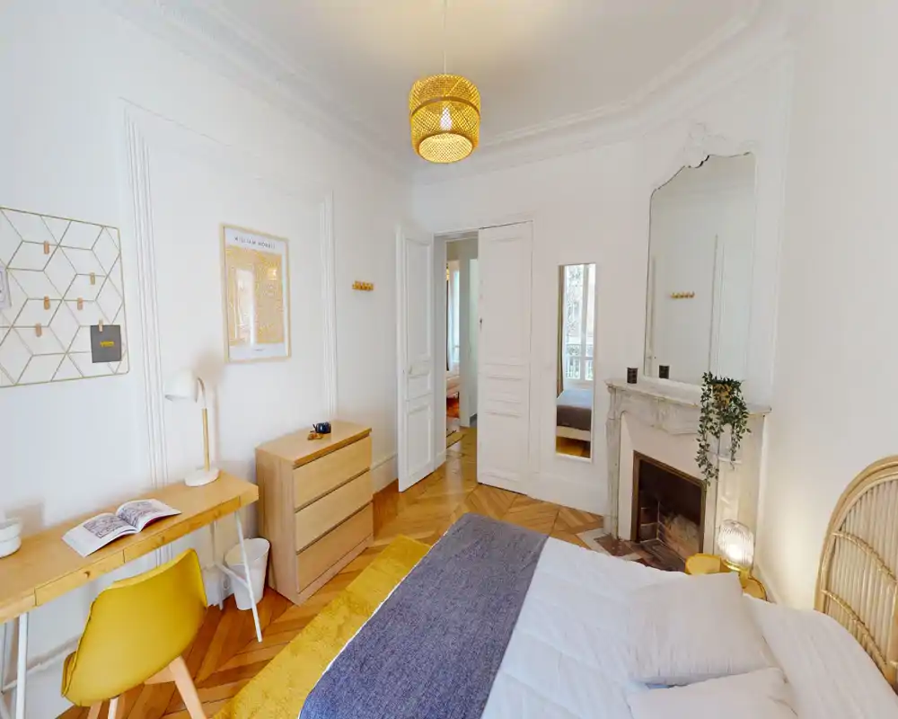 Dormitorio luminoso y estilo nórdico con cabecero de ratán, suelo de madera en espiga y detalles cálidos; cama doble cómoda, zona de escritorio y chimenea decorativa.