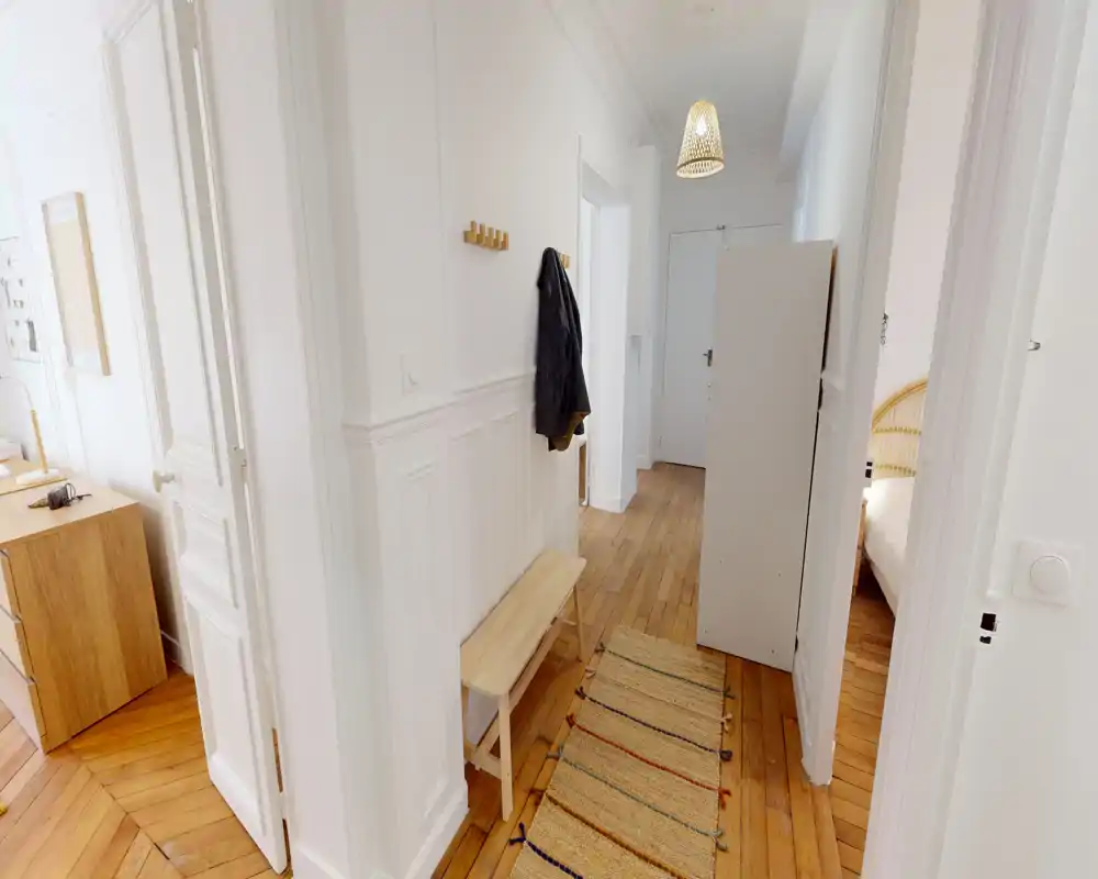 Vestíbulo luminoso y estrecho con suelos de madera, un banco pequeño y perchas en la pared — acceso limpio y acogedor a las habitaciones contiguas.