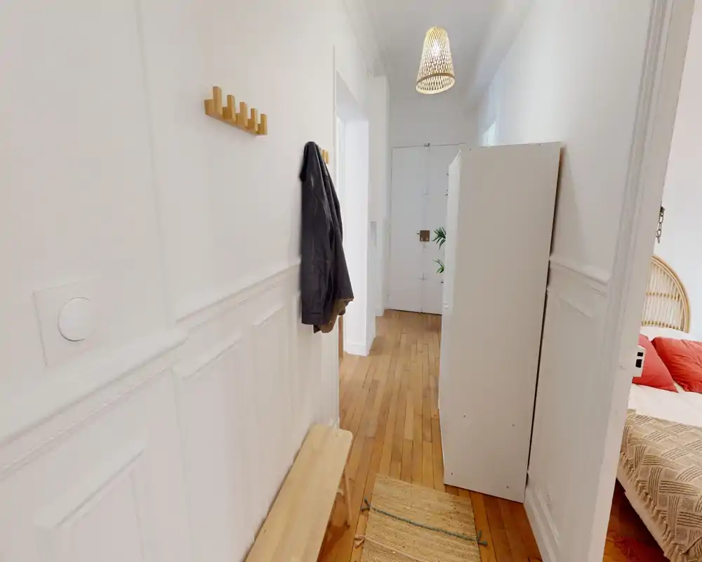 Recibidor luminoso y ordenado con suelo de madera, molduras en la pared, percheros y banco — espacio de entrada práctico que conduce a otras estancias.