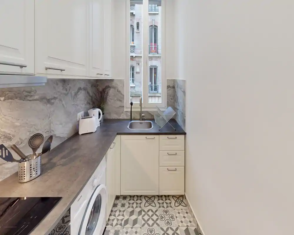 Cocina compacta y luminosa con suelo de baldosas estampadas, muebles claros, fregadero integrado y pequeños electrodomésticos: ideal para un piso pequeño.