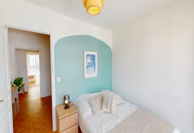 Cozy bright single bedroom with a mint accent wall, soft bedding and a wooden nightstand. The room is well lit and staged for a comfortable stay, ideal for a solo traveler.