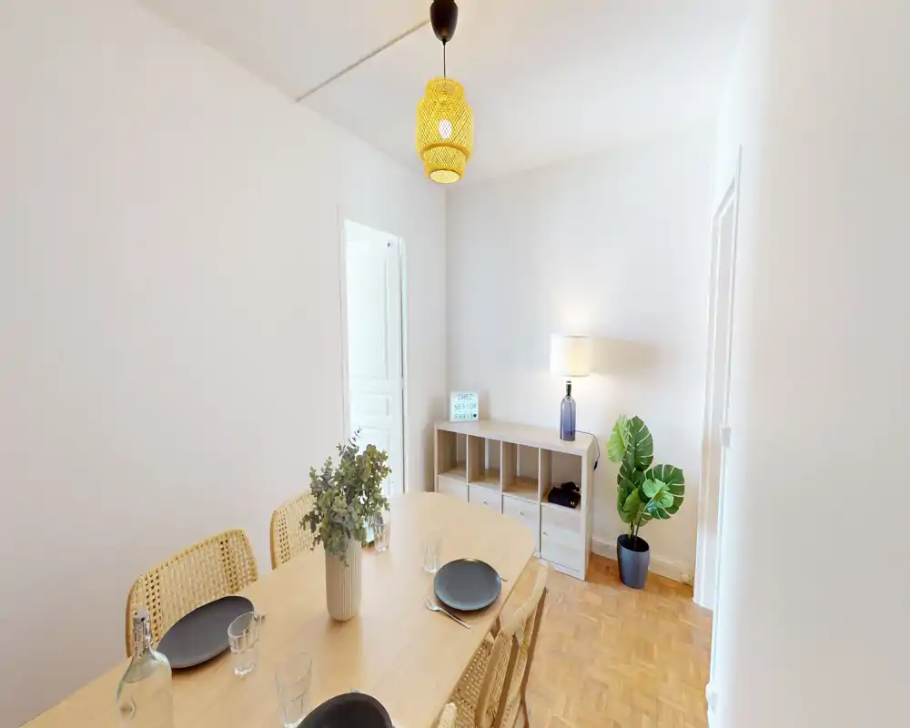 Bright, stylish dining area with a wooden table set for four, rattan chairs and soft ambient lighting — ideal for cozy meals.