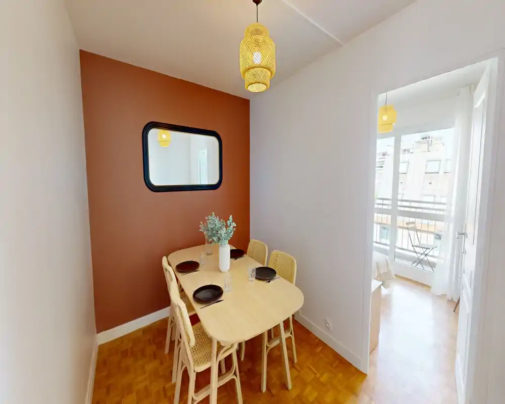Cozy dining nook with a wooden table for four, woven chairs and a warm terracotta accent wall. Natural light from the adjacent room and a pendant lamp create a bright, inviting atmosphere.
