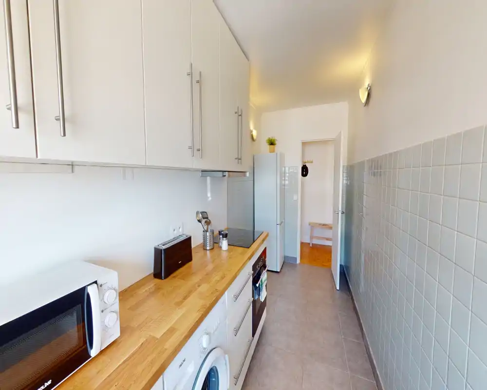 Bright, narrow kitchen with wood countertop, white cabinets, microwave and built-in appliances — neat and well-lit space ideal for compact apartments.