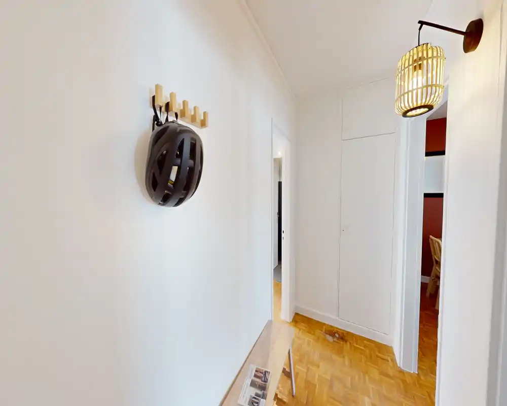 Bright, tidy entry hallway with wooden parquet flooring, a wall-mounted coat hook with a helmet, a small bench with reading material and built-in closet doors — perfect first impression for a rental.