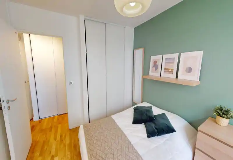 Bright, neatly staged bedroom with a double bed dressed in white linens, green accent wall, decorative shelf art and a small dresser — ideal for rental listings.