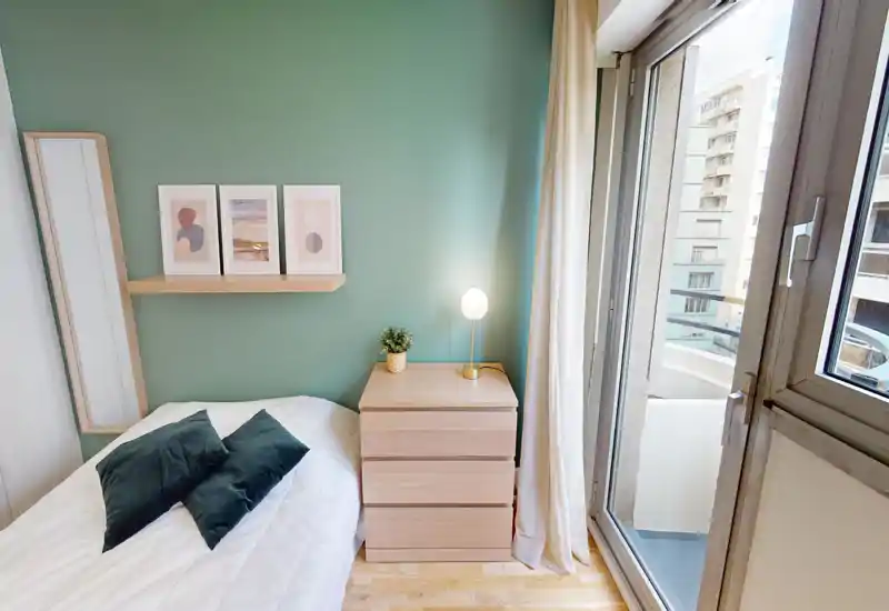 Bright, well-staged bedroom with a comfortable bed, bedside chest, decorative pillows and direct access to a small balcony letting in abundant natural light.