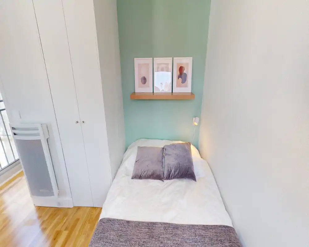 Chambre compacte, bien mise en scène avec un lit double central, coussins doux et un mur d'accent menthe orné de cadres. Lumière naturelle abondante et parquet propre donnent une atmosphère accueillante.