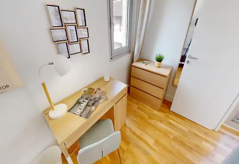 Compact, bright room staged with a wooden desk, chair and chest of drawers — ideal for a study corner within a small bedroom or studio.