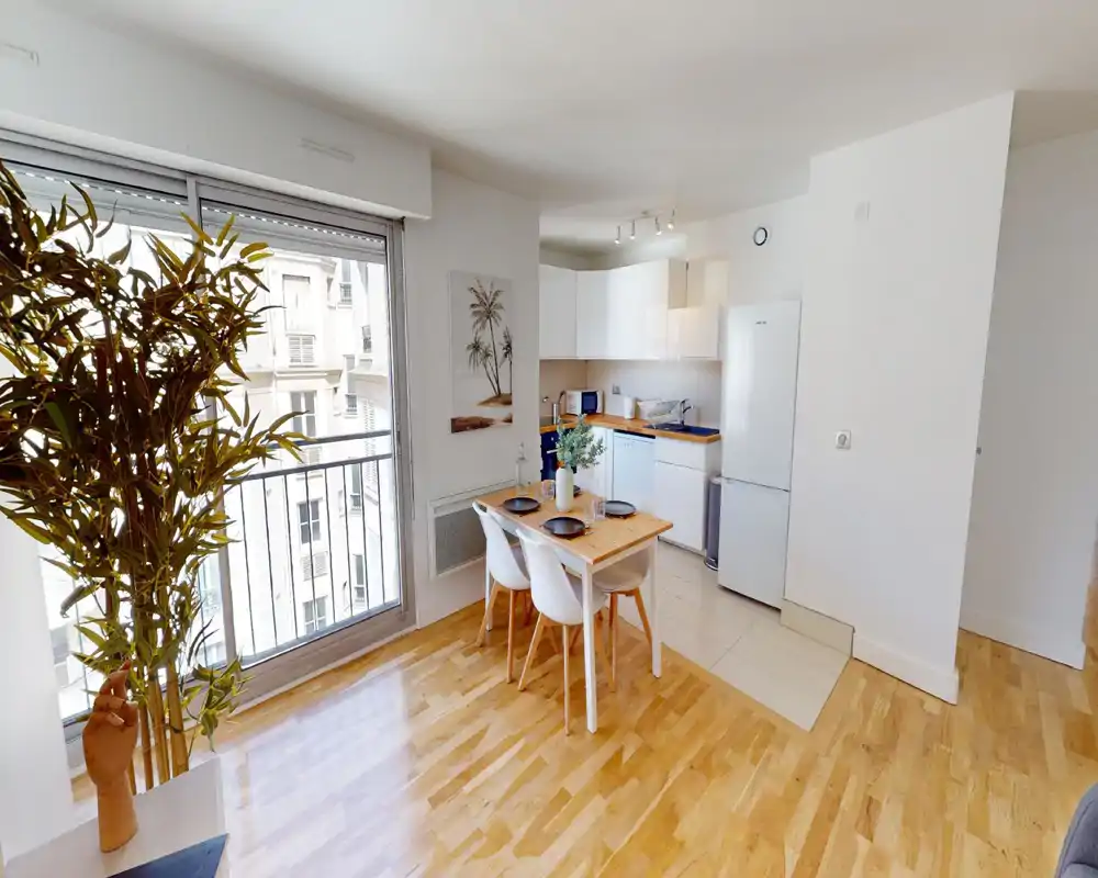 Bright open-plan kitchen with a compact dining table. White cabinets, wooden countertops and a large window provide a fresh, modern feel ideal for a city rental.