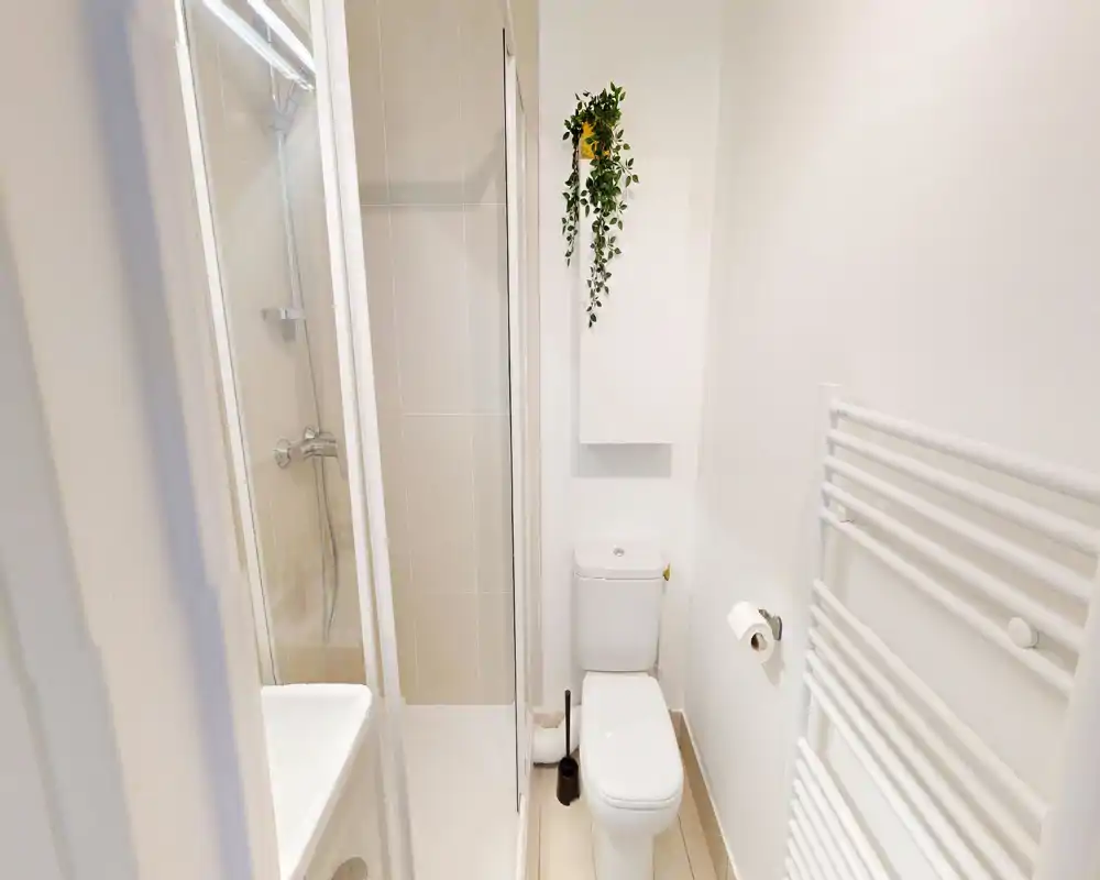 Compact, modern bathroom with a shower cabin, toilet and heated towel radiator; bright white tiles and fixtures create a clean, minimal look.