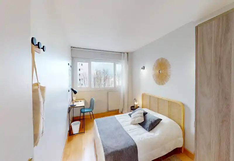 Camera da letto luminosa e ben arredata con testiera in rattan, letto matrimoniale rifatto e una scrivania vicino alla finestra — ideale per soggiorni confortevoli o monolocali per studenti.
