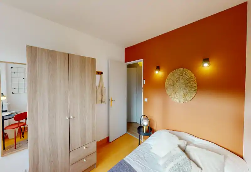 Chambre chaleureuse et lumineuse avec un mur d'accent terracotta, des appliques au-dessus du lit et un lit confortable avec coussins — idéale pour une annonce locative.