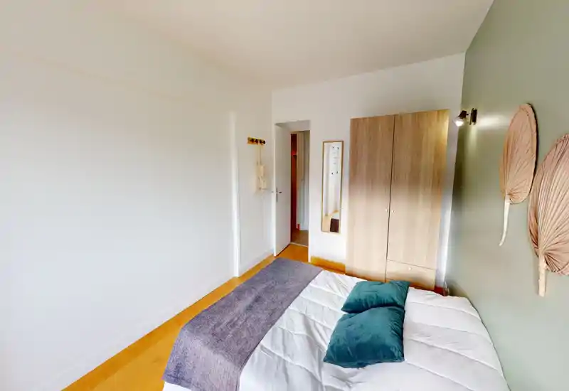 Chambre lumineuse au style épuré avec lit double, mur vert et armoire en bois ; textiles et coussins donnent une atmosphère confortable.