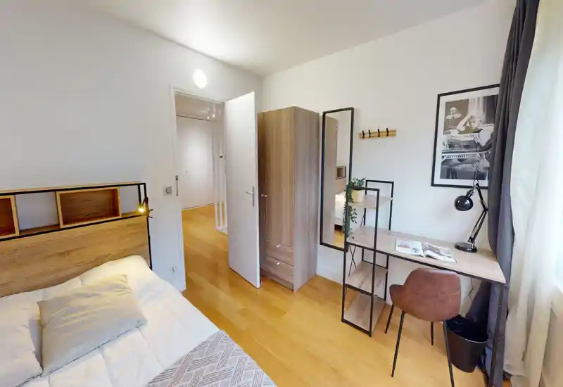 Bright, well-styled bedroom with a wooden headboard, bedside lamp and a workspace by the window. Natural light and warm flooring create a welcoming atmosphere.