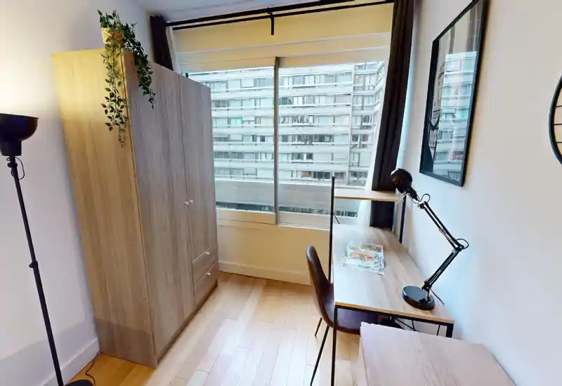 Dormitorio luminoso con gran ventana, armario de madera y una mesa compacta ideal para teletrabajo; decoración moderna y buena luz natural.