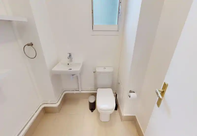 Compact, bright bathroom with a wall-mounted sink and a toilet; neutral tiles and white walls create a clean, minimal look.