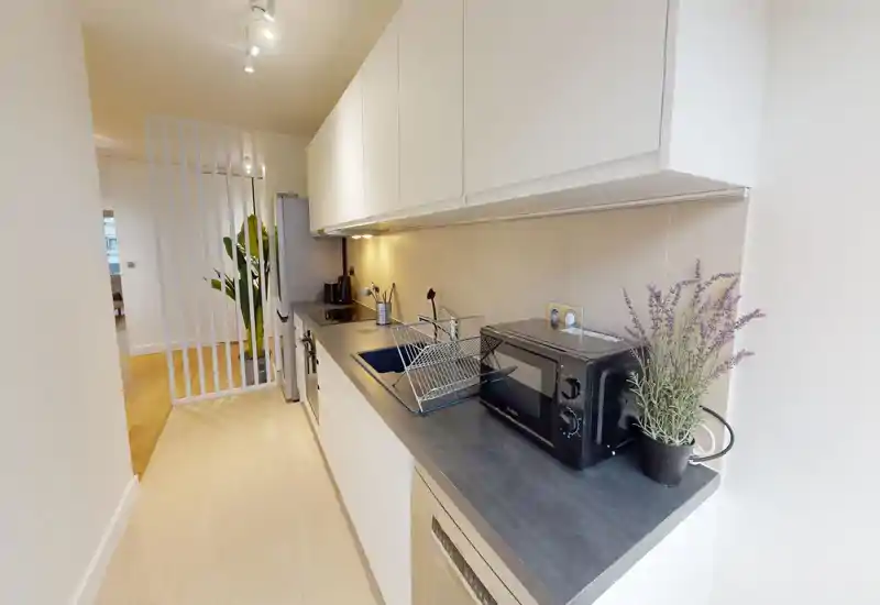 Modern galley kitchen with white cabinetry, dark countertop and built-in appliances; neat layout with microwave, sink and under-cabinet lighting.