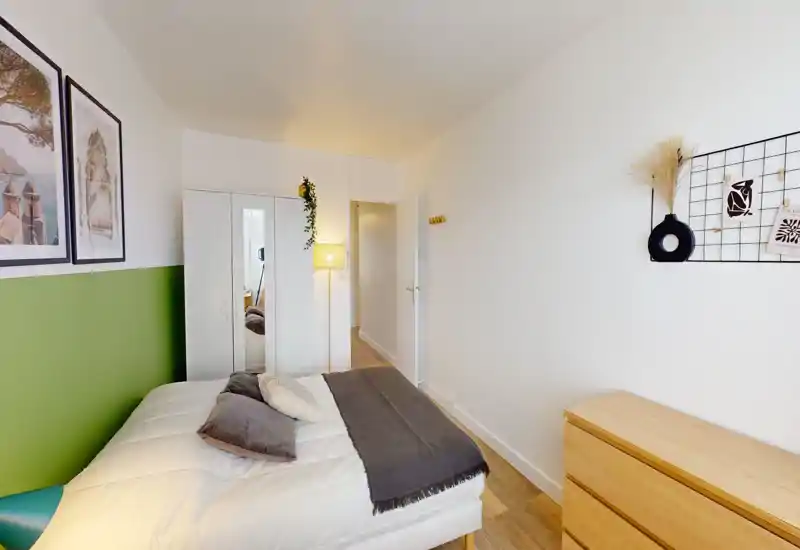 A bright, neatly staged bedroom with a double bed, decorative pillows and a wardrobe with mirrored doors. Neutral walls with a green accent and wooden flooring create a calm, modern feel.