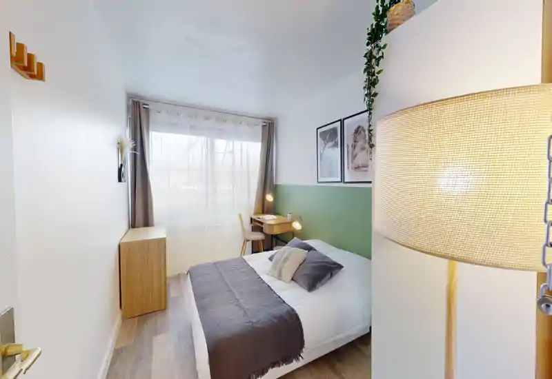 Bright, well-styled bedroom with a double bed, bedside cushions, a small writing desk by the window and warm lighting — ideal for a comfortable short stay.
