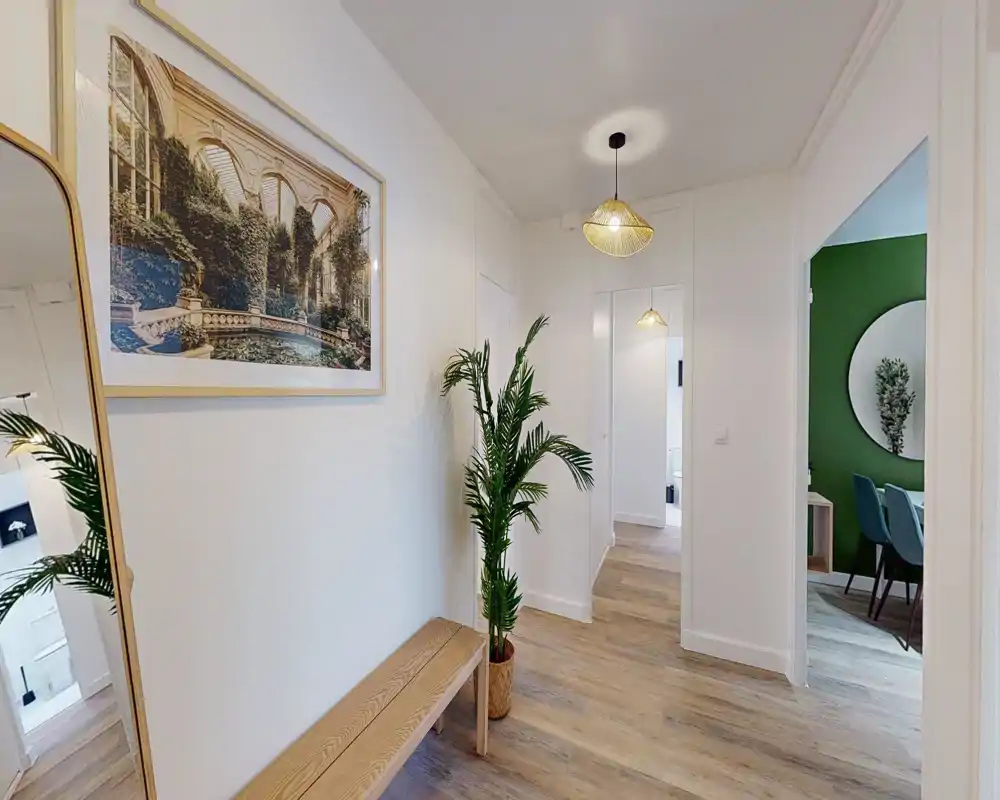 Bright, neatly staged entrance hallway with wooden bench, large wall mirror and decorative plant, leading to adjacent rooms.