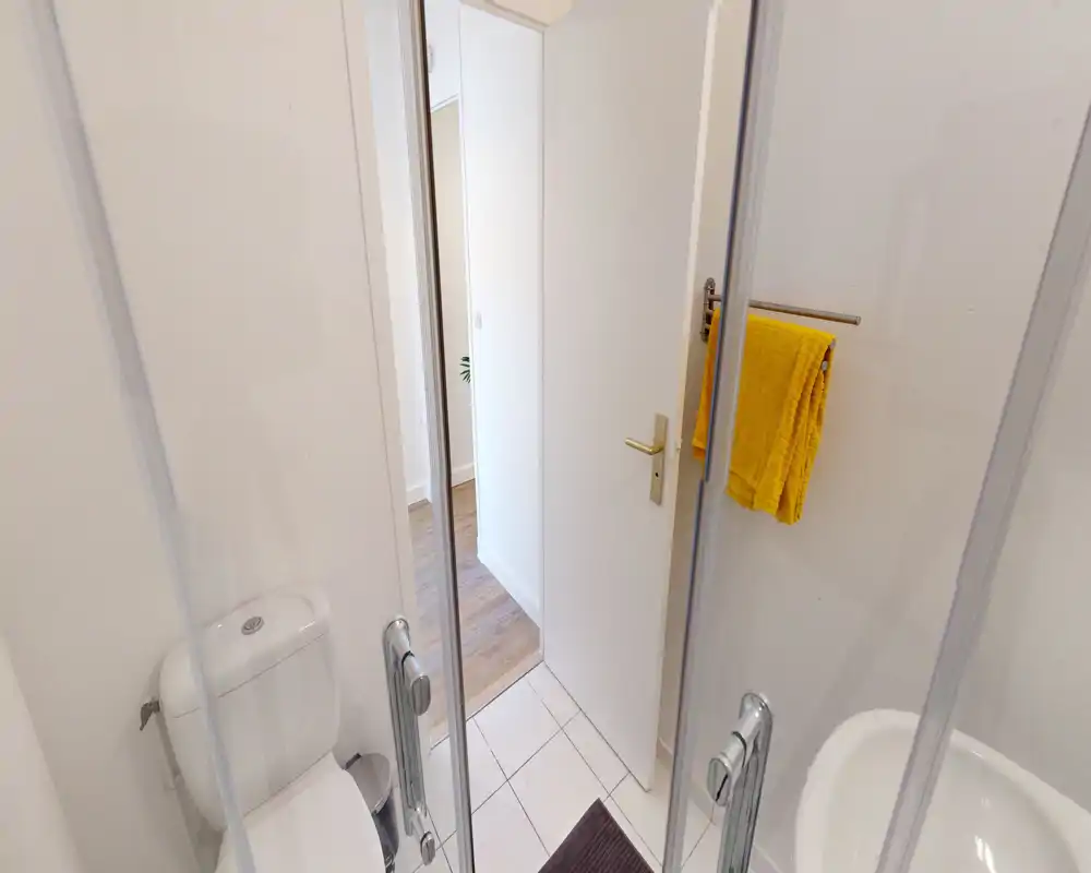Compact, clean bathroom with tiled floor, toilet, sink and a glass shower door; bright and neatly presented.
