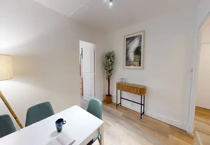 Bright, modern living area with a small dining table, upholstered chairs, a floor lamp and tasteful wall art — ideal for a compact apartment living/dining corner.