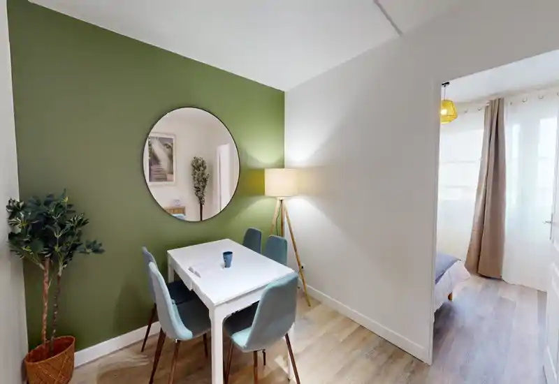 Bright, styled dining nook with a white table, four upholstered chairs and decorative mirror on a green accent wall — a cozy spot for meals or work.