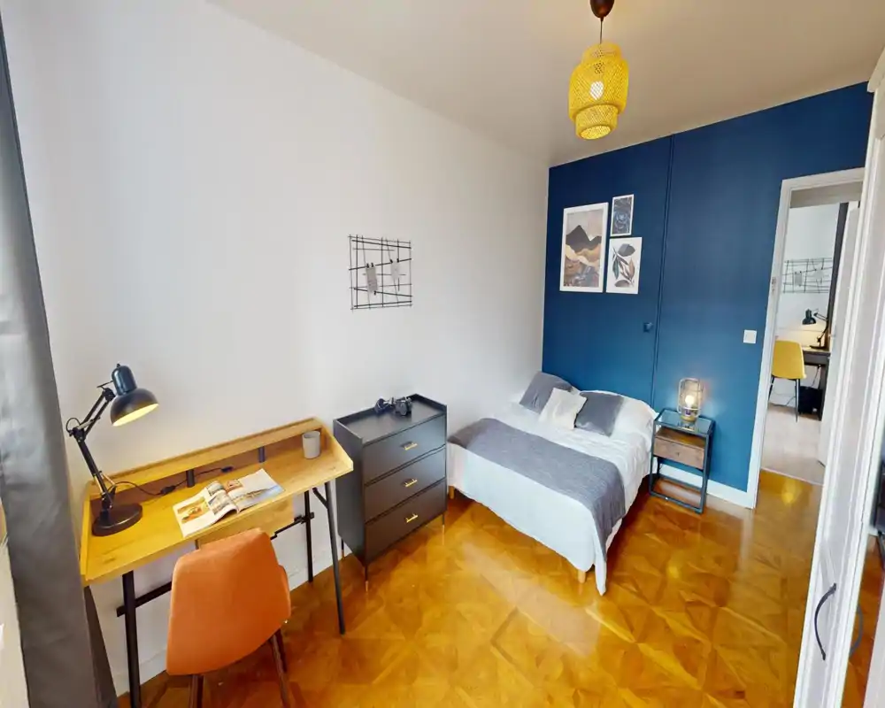 Chambre lumineuse et stylée avec un lit double contre un mur accent bleu marine, table de chevet et un petit bureau parfait pour le télétravail. Parquet chaleureux et décoration coordonnée créent une atmosphère accueillante.
