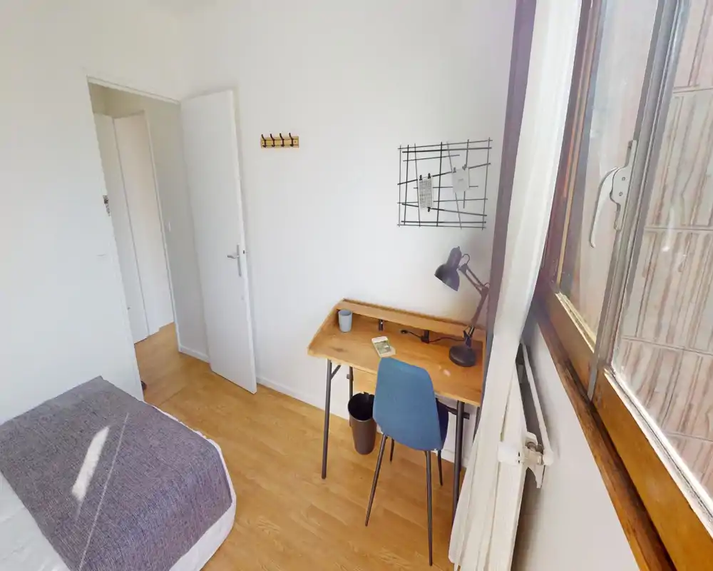 Camera da letto luminosa e ordinata con letto singolo e scrivania in legno vicino alla finestra — ideale per uno studente o un professionista. La luce naturale rende l'ambiente accogliente e funzionale.
