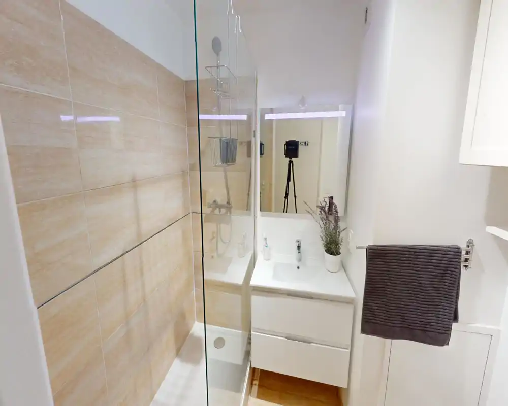 Salle de bains moderne et lumineuse avec douche à l'italienne, paroi en verre et meuble vasque blanc avec miroir.